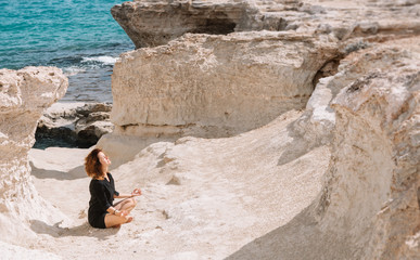 Beautiful woman meditates and relax in the rocks near the sea.