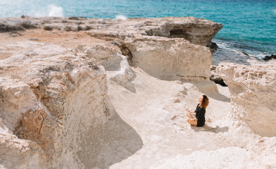 Beautiful woman meditates and relax in the rocks near the sea.