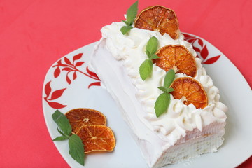 Sponge cream cake coated with cream and garnished with dried orange slices and fresh mint leaves. Against the background of coral color.