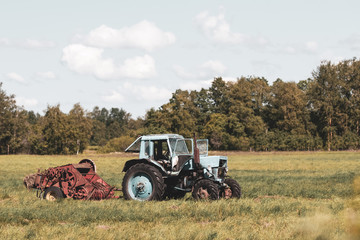 Fototapeta premium Old soviet tractor with assembly in the field. There is not anyone. There are clouds in the sky. Away the forest.