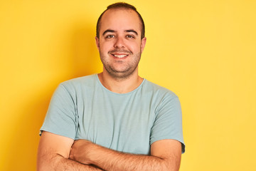 Fototapeta premium Young man wearing green casual t-shirt standing over isolated yellow background happy face smiling with crossed arms looking at the camera. Positive person.