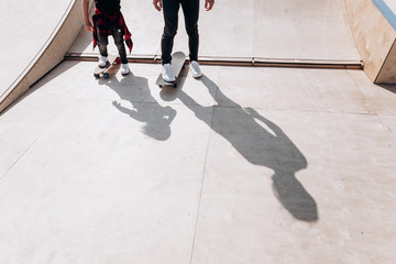 Father and his little son dressed in the casual clothes ride skateboards in a skate park with slides at the sunny day