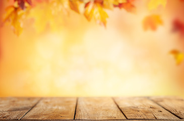 Naklejka na ściany i meble Wooden table and blurred Autumn background. Autumn concept with red-yellow leaves background.