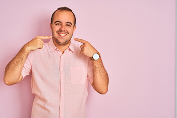Young man wearing elegant shirt standing over isolated pink background smiling cheerful showing and pointing with fingers teeth and mouth. Dental health concept.