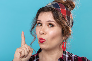 Cute young woman in a plaid shirt showing thumbs up posing against a blue background. Concept of...