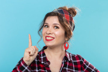 Cute young woman in a plaid shirt showing thumbs up posing against a blue background. Concept of...