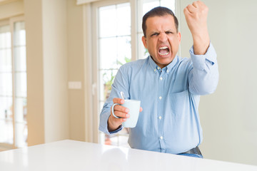 Middle age man drinking coffee in the morning at home annoyed and frustrated shouting with anger, crazy and yelling with raised hand, anger concept