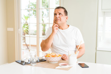 Middle age man eating asian food with chopsticks at home with hand on chin thinking about question, pensive expression. Smiling with thoughtful face. Doubt concept.