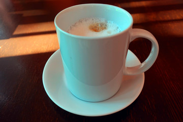 white porcelain cup with hot cappuccino on a saucer