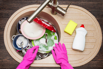 Close up hands of woman washing dishes in kitchen. Hands in red rubber gloves washing the dishes. Top view
