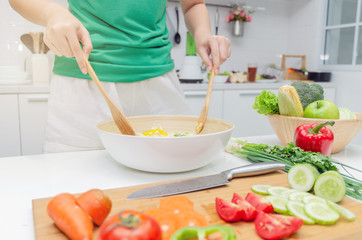 Obraz na płótnie Canvas Diet. young pretty woman in green shirt standing and preparing the vegetables salad in bowl for good healthy in modern kitchen at home, healthy lifestyle, cooking, healthy food and dieting concept