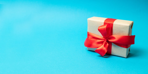 Craft paper present with red ribbon on blue background. Square shot