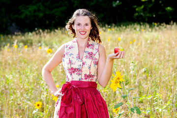 woman in dirndl standing in field of flowers and holding an apple