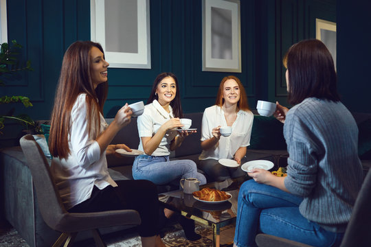 Women drink coffee laughing at a meeting of friends at home.
