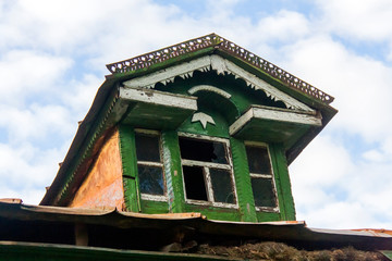 decrepit dormer-window on the roof of a wooden Russian hut on a summer day under a blue sky