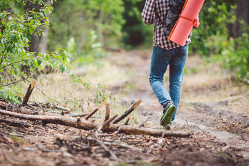 Concept breathtaking journey and adventure. Back view hike brave Caucasian guy with backpack walks into forest along country road. Theme tourism and outdoor activities. backpacker goes through forest