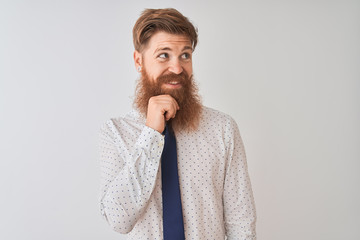 Young redhead irish businessman standing over isolated white background with hand on chin thinking about question, pensive expression. Smiling and thoughtful face. Doubt concept.