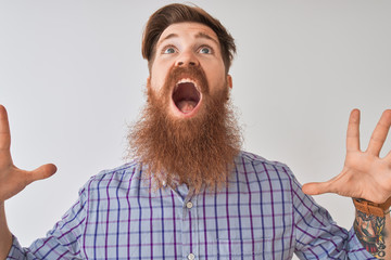Redhead irish man listening to music using wireless earphones over isolated white background crazy and mad shouting and yelling with aggressive expression and arms raised. Frustration concept.