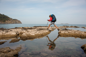 Girl jumping on the rocks on the sea with hiking backpack