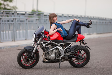 Fototapeta na wymiar biker woman lying on a vintage motorcycle. Girl with perfect fit slim body. The spirit of freedom and independence. Beautiful brave woman is leaning on her cafe racer motobike on highway