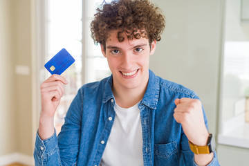 Young man holding credit card screaming proud and celebrating victory and success very excited, cheering emotion