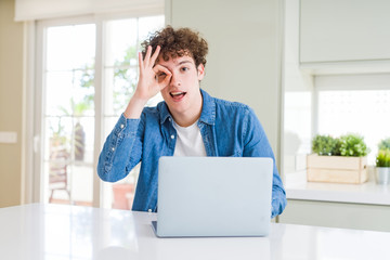 Young man using computer laptop with happy face smiling doing ok sign with hand on eye looking through fingers