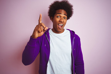 Young african american man wearing purple sweatshirt standing over isolated pink background pointing finger up with successful idea. Exited and happy. Number one.