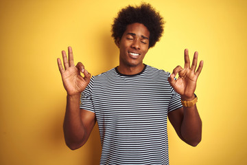 African american man with afro hair wearing navy striped t-shirt over isolated yellow background relax and smiling with eyes closed doing meditation gesture with fingers. Yoga concept.