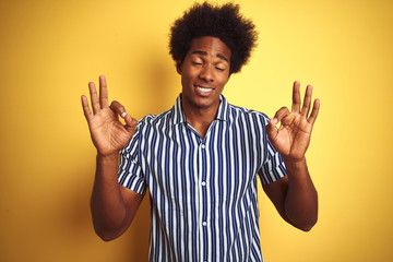 American man with afro hair wearing striped shirt standing over isolated yellow background relax and smiling with eyes closed doing meditation gesture with fingers. Yoga concept.