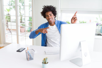 African American man working using computer smiling and looking at the camera pointing with two hands and fingers to the side.