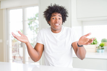 Fototapeta na wymiar Young african american man wearing casual white t-shirt sitting at home clueless and confused with open arms, no idea concept.