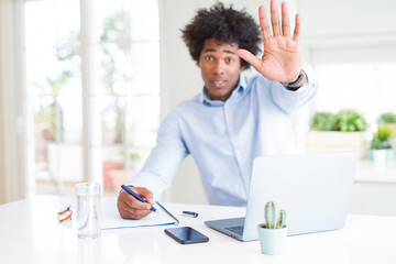 African American business man working writing on notebook with open hand doing stop sign with...