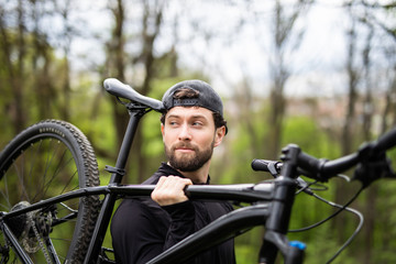 Happy handsome biker holding bike and looking at camera in the nature