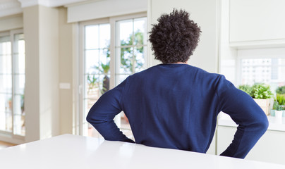 Young african american man wearing casual sweater sitting at home standing backwards looking away with arms on body