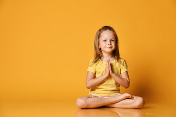 Smiling girl practicing yoga, sitting in the lotus position with legs crossed, preparing for...
