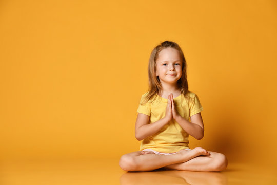 Smiling girl practicing yoga, sitting in the lotus position with legs crossed, preparing for training, working out wearing sportswear, t-shirts, pants, yellow studio background