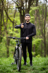 Happy man shows thumb up, riding on bicycle in forest, sport leisure. Cyclist walk in park, active...