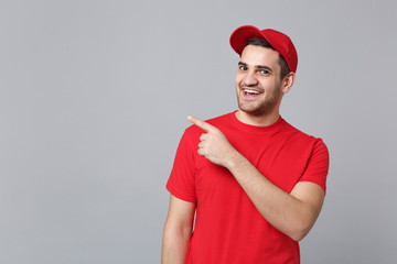 Delivery man in red uniform workwear isolated on grey wall background, studio portrait. Professional male employee in cap t-shirt print working as courier dealer. Service concept. Mock up copy space.