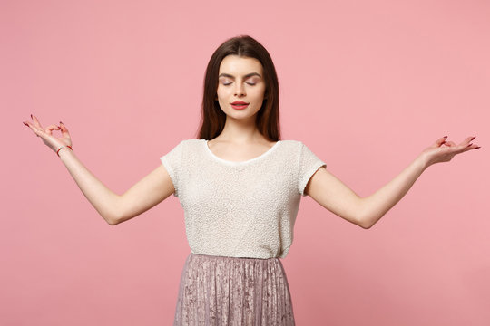 Relaxed young woman in casual light clothes posing isolated on pastel pink background. People lifestyle concept. Mock up copy space. Hold hands in yoga gesture relaxing meditating keeping eyes closed.