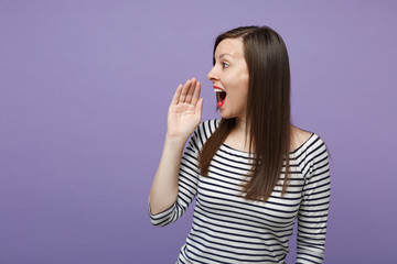 Excited young woman in casual striped clothes posing isolated on violet purple background in studio. People lifestyle concept. Mock up copy space. Looking aside screaming with hand gesture near mouth.