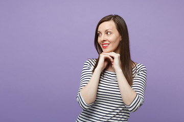 Attractive young woman in casual striped clothes posing isolated on violet purple background studio portrait. People lifestyle concept. Mock up copy space. Looking aside, put hands prop up on chin.