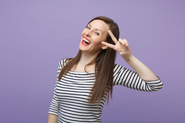 Laughing cheerful young brunette woman girl in casual striped clothes posing isolated on violet purple background studio portrait. People lifestyle concept. Mock up copy space. Showing victory sign.