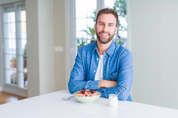 Handsome man eating cereals for breakfast at home with a happy and cool smile on face. Lucky person.