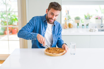 Handsome man cutting a pizza slice at home