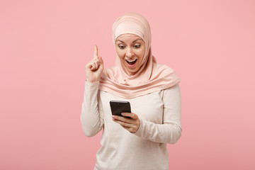 Arabian muslim woman in hijab light clothes posing isolated on pink background. People religious lifestyle concept. Mock up copy space. Typing sms message, holding index finger up with great new idea.