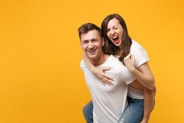 Young couple in white t-shirt posing isolated on yellow orange background. People lifestyle concept. Mock up copy space. Giving piggyback ride to joyful sitting on back doing winner gesture screaming.