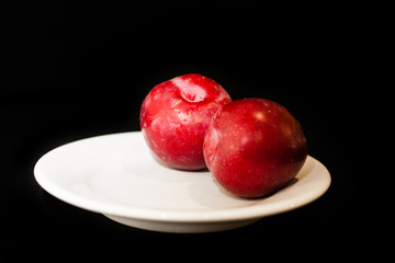 Fototapeta na wymiar Frutas ciruelas en plato y fondo negro