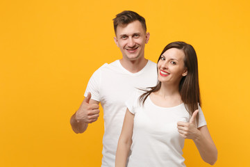 Beautiful smiling young couple two friends guy girl in white empty blank design t-shirts posing isolated on yellow orange background. People lifestyle concept. Mock up copy space. Showing thumbs up.