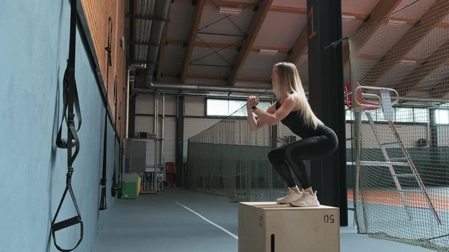 Young strong woman with perfect fitness body in sportswear doing set of box jumps at gym in slow motion. Athletic female does box jumps indoors. Full length shot. Wide angle
