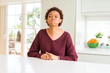 Young beautiful african american woman at home puffing cheeks with funny face. Mouth inflated with air, crazy expression.